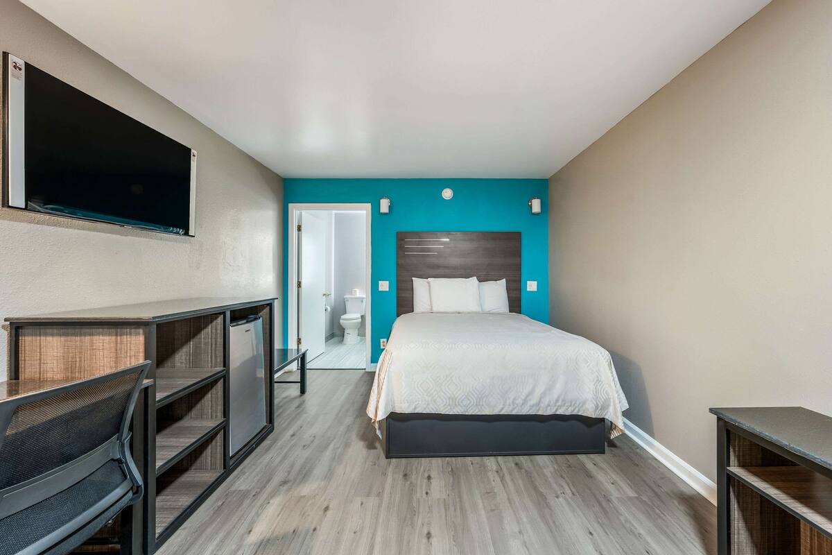 A hotel room with a bed, a TV, a desk, and a bathroom visible through an open door.