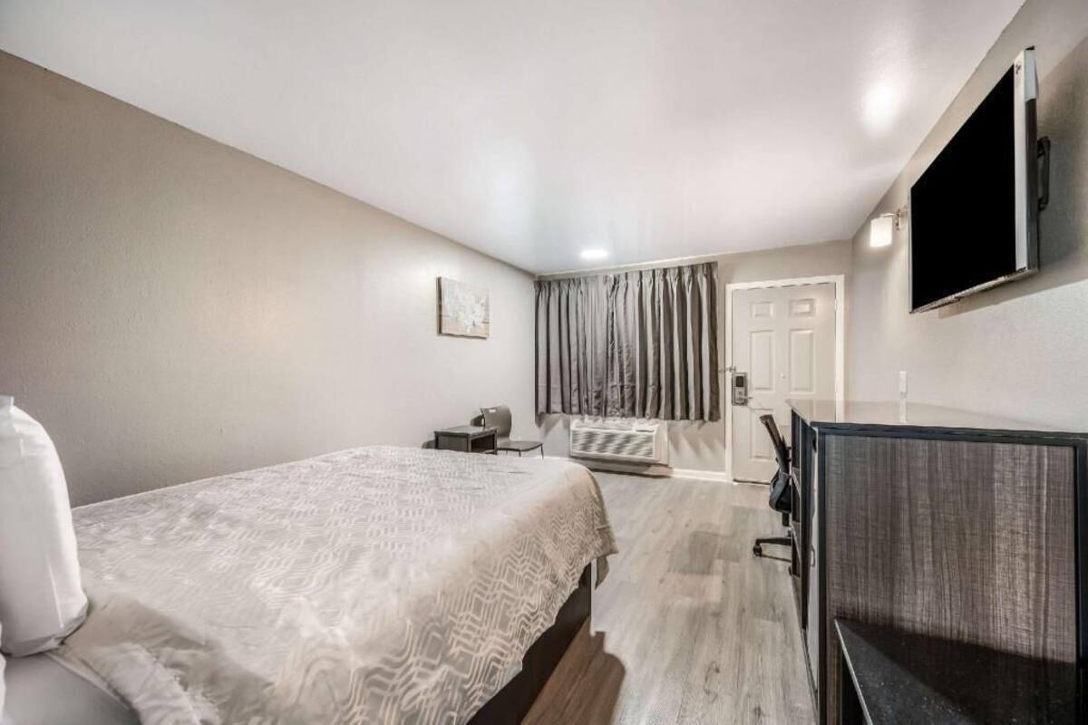 A hotel room with a bed, desk, chair, TV, and curtains.