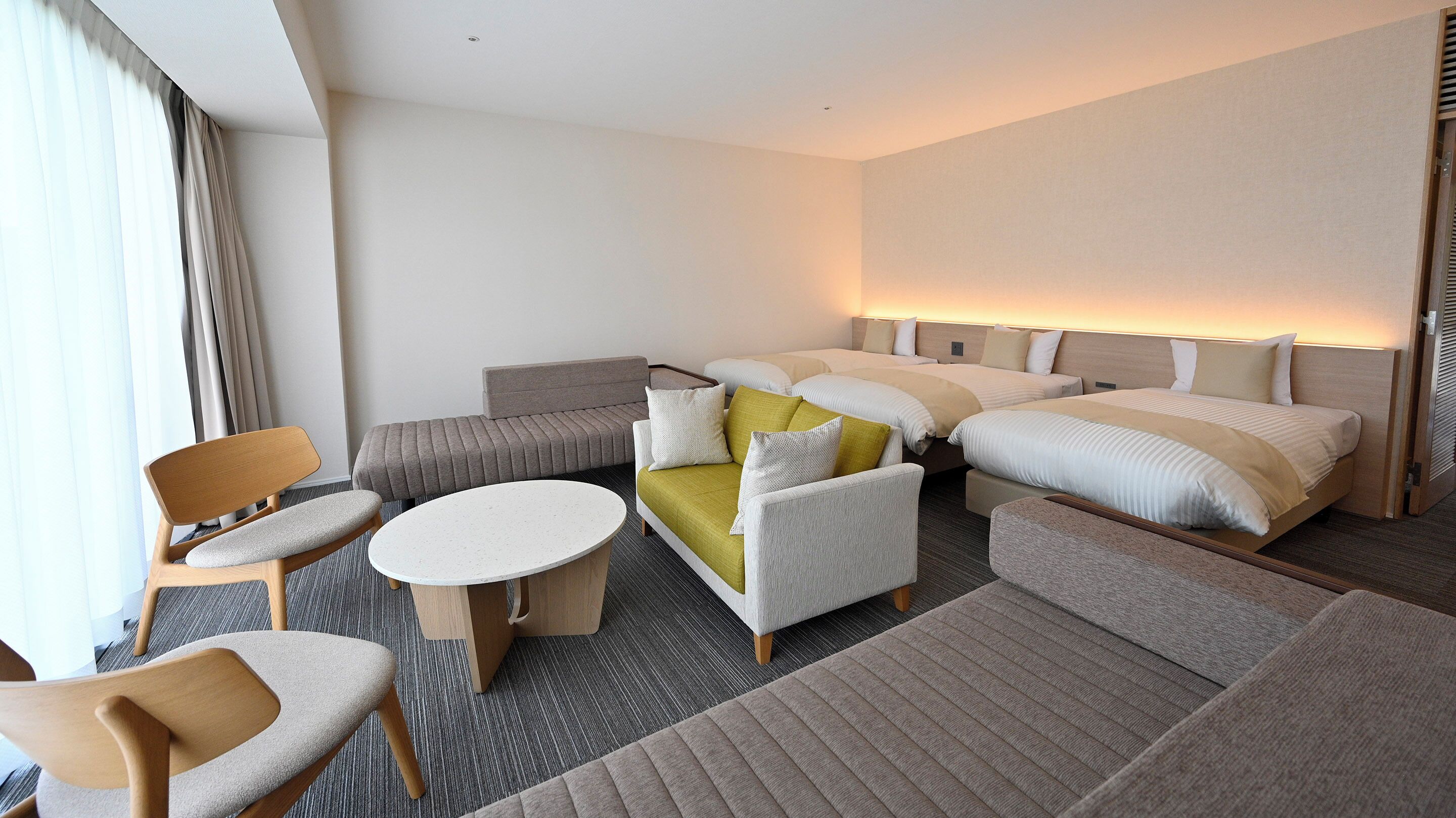 A hotel room with a bed, sofa, chairs, a small table, and a carpeted floor.