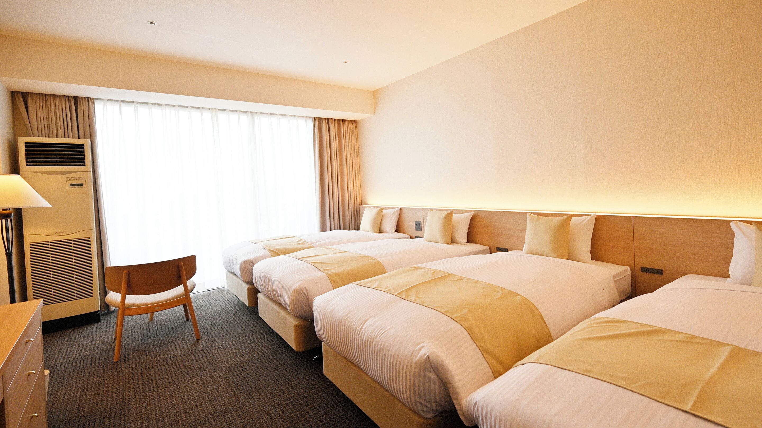 A hotel room with two beds, a desk, a chair, and a window with curtains.