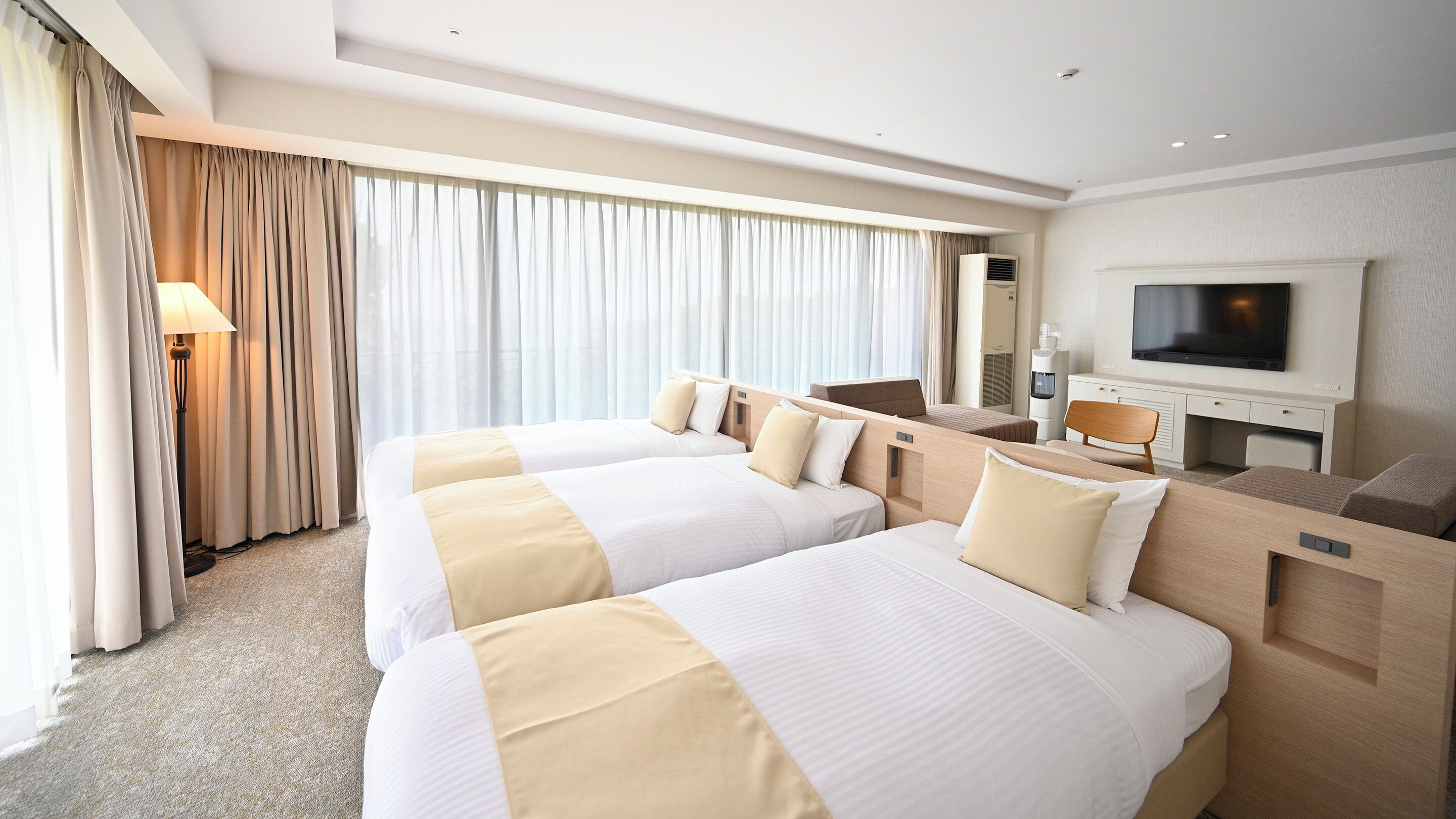 A hotel room with two beds, a TV, a desk, and a large window with curtains.