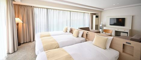 A hotel room with two beds, a TV, a desk, and a large window with curtains.