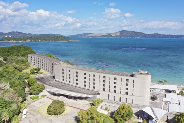 A modern building with a flat roof, surrounded by greenery and a large body of water.