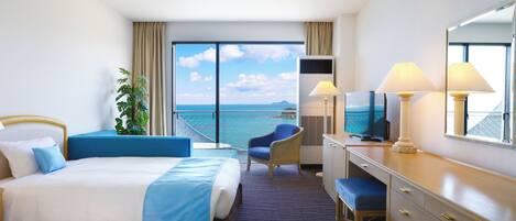 A hotel room with two beds, a desk, a chair, a TV, and a large window with a view of the sea.