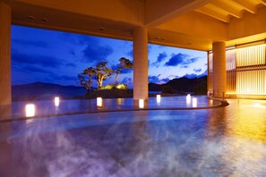 A spacious indoor area with a view of trees and mountains at dusk.
