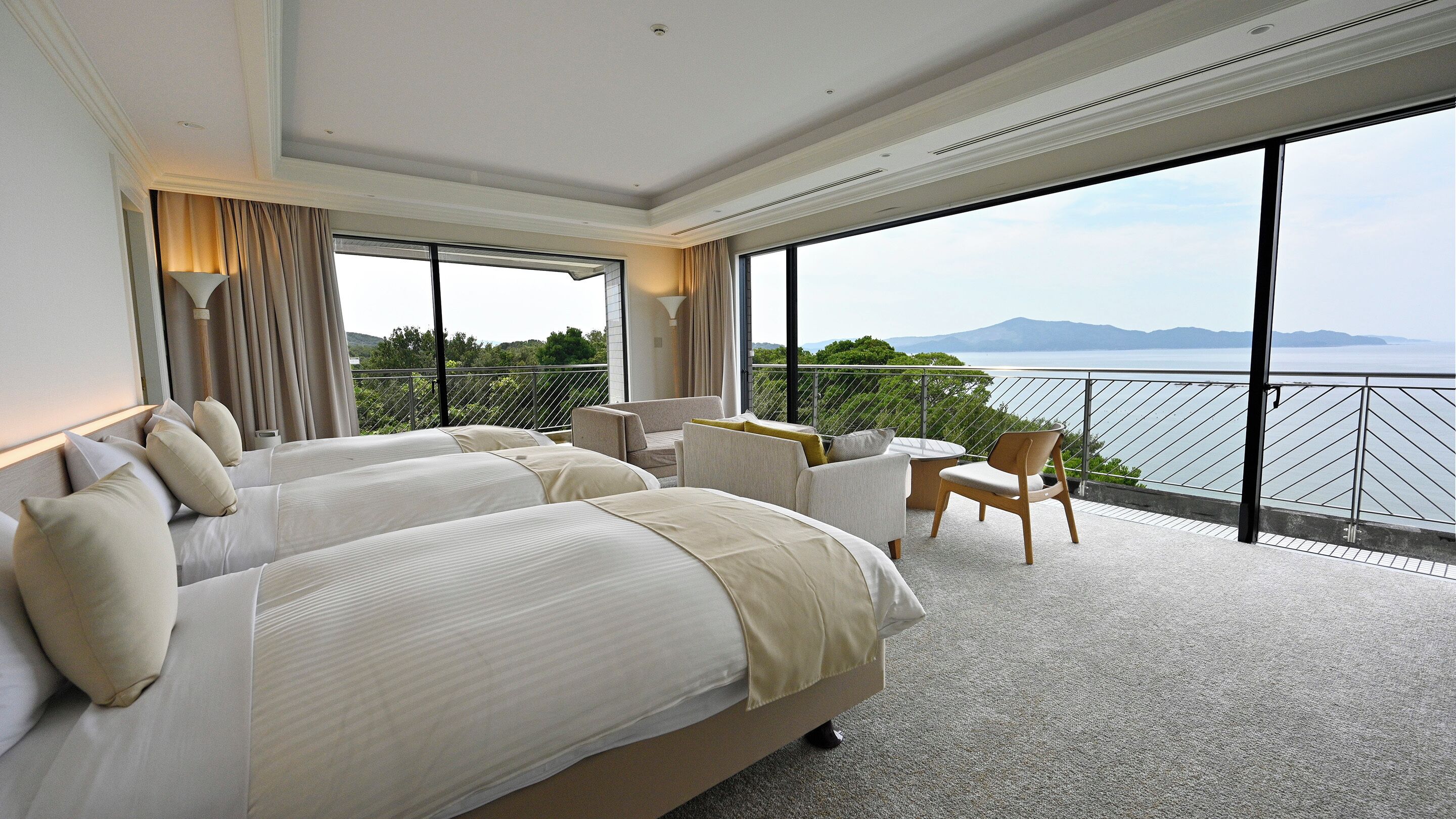 A hotel room with two beds, a balcony with a view of the sea, and a dining area.