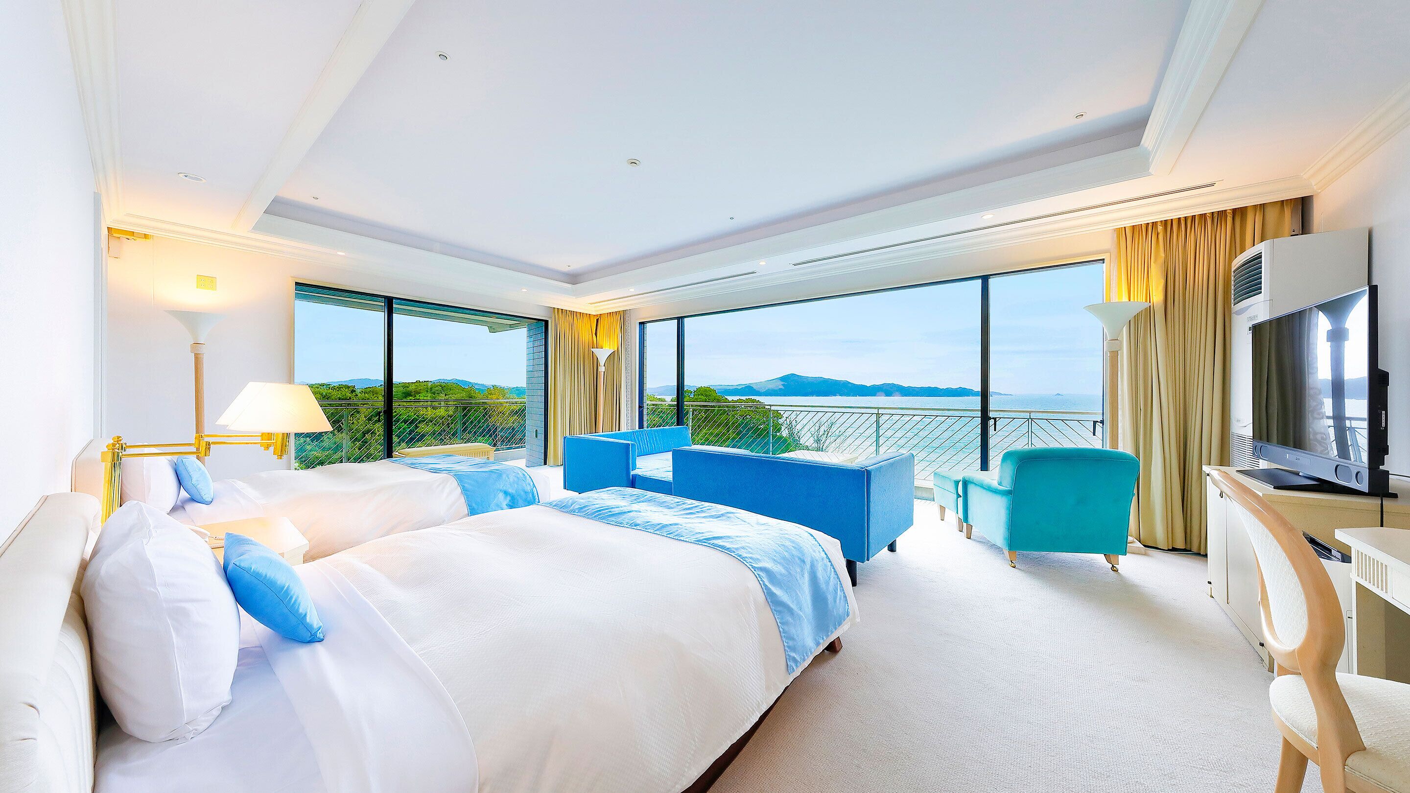 A hotel room with a large bed, a desk, a TV, and a balcony with a view.