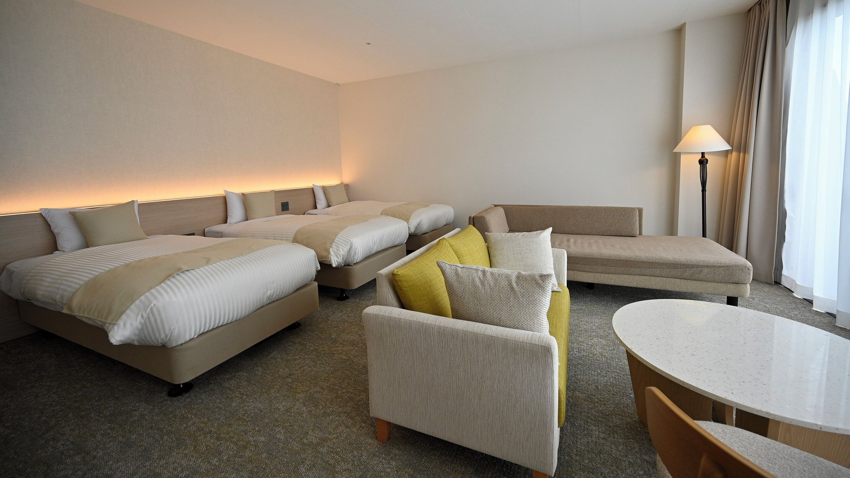 A hotel room with three beds, a sofa, a small table, and a lamp.