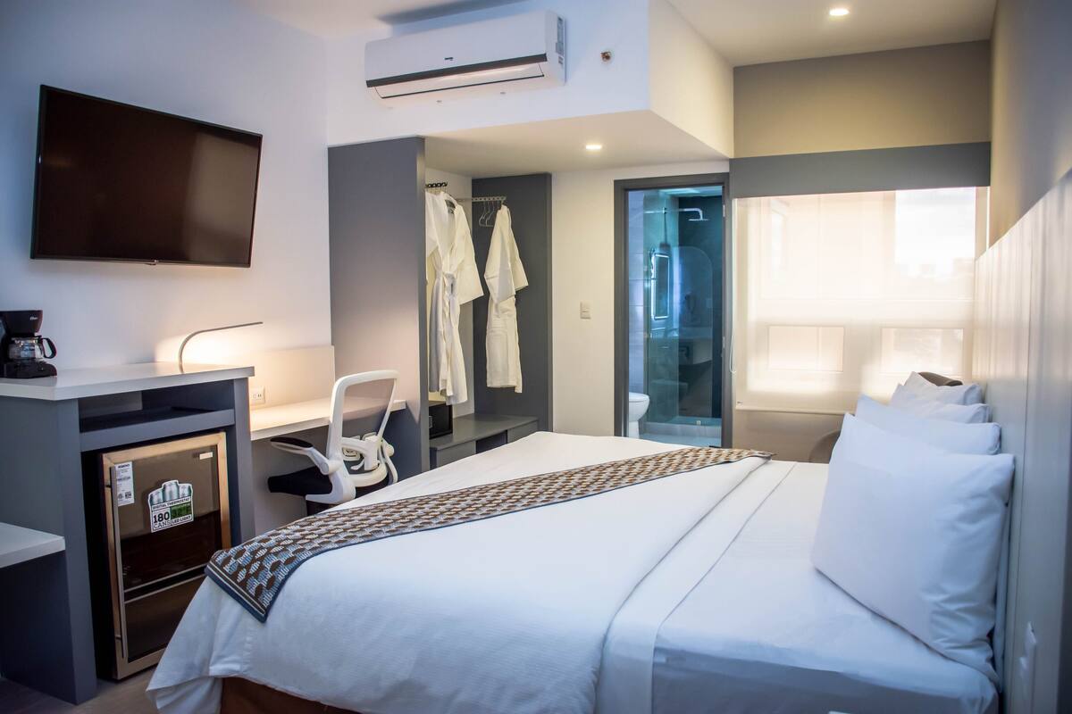 Hotelkamer met een bed, bureau, stoel, televisie en een douche.