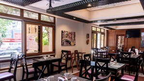 A restaurant with multiple tables and chairs, large windows, and a painting on the wall.