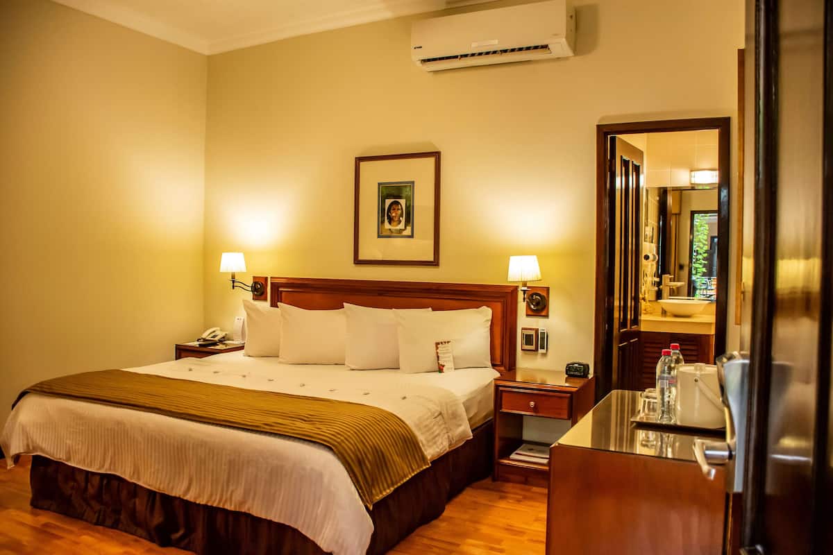 Een hotelkamer met een groot bed, nachtlampjes, een nachtkastje, een spiegel en een houten dressoir.