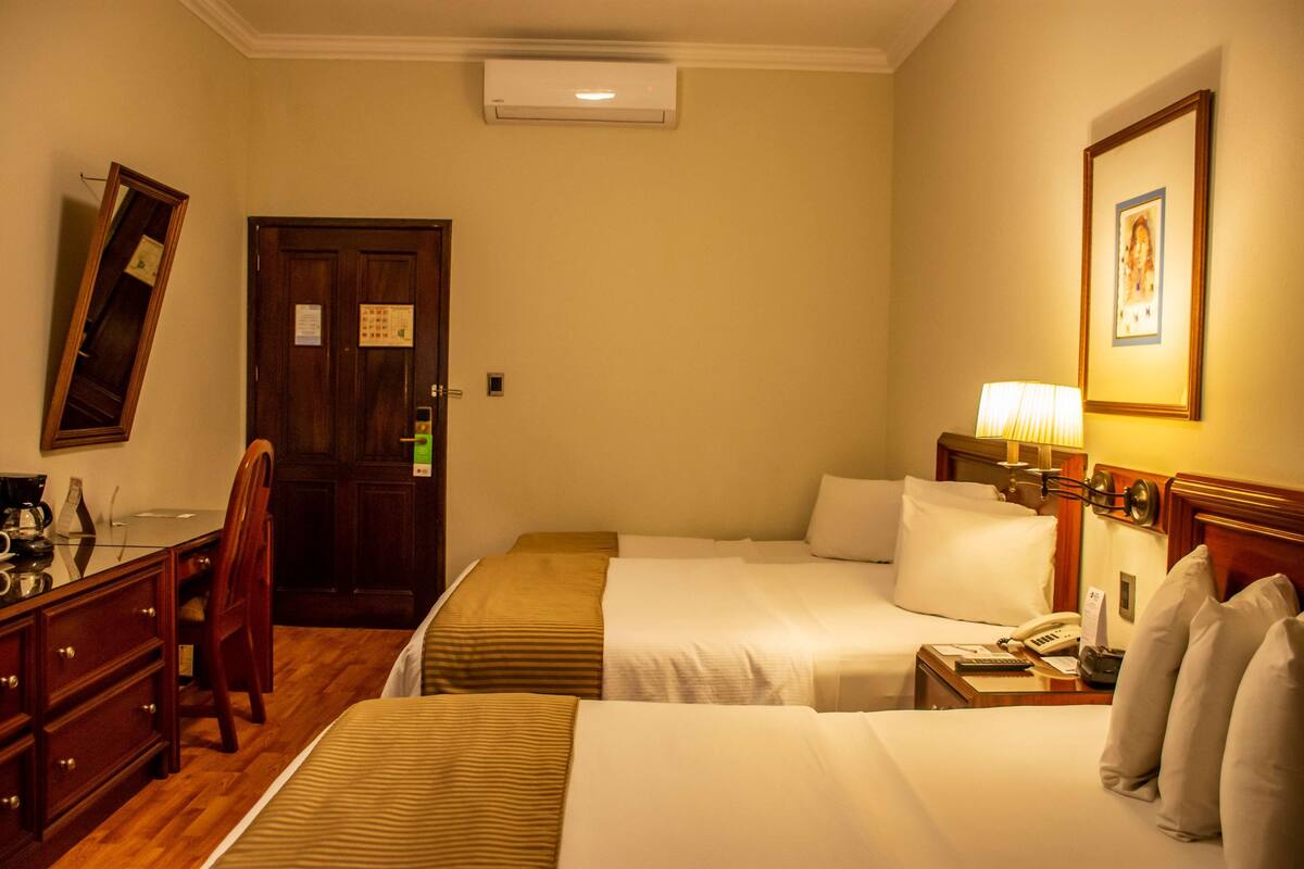 Een hotelkamer met twee bedden, een bureau, een stoel, een lamp en een lijst aan de muur.