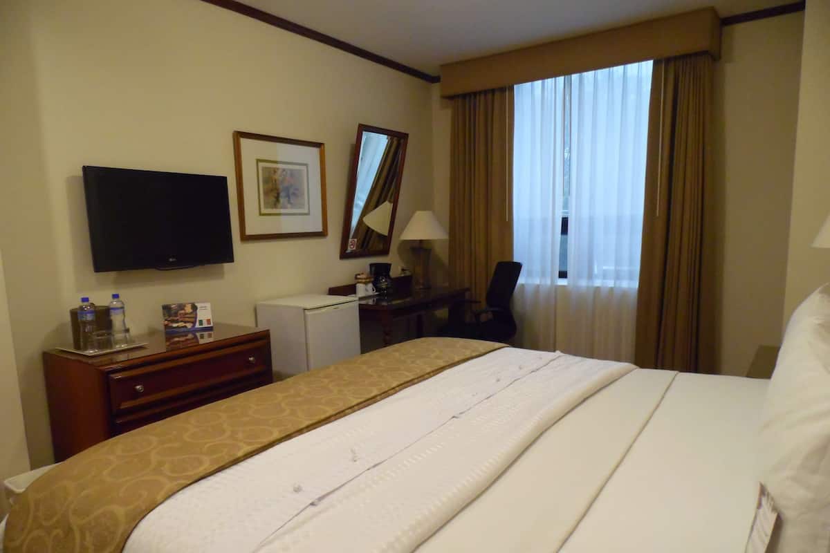 Een hotelkamer met een bed, een bureau, een televisie, een koelkast en een raam met gordijnen.