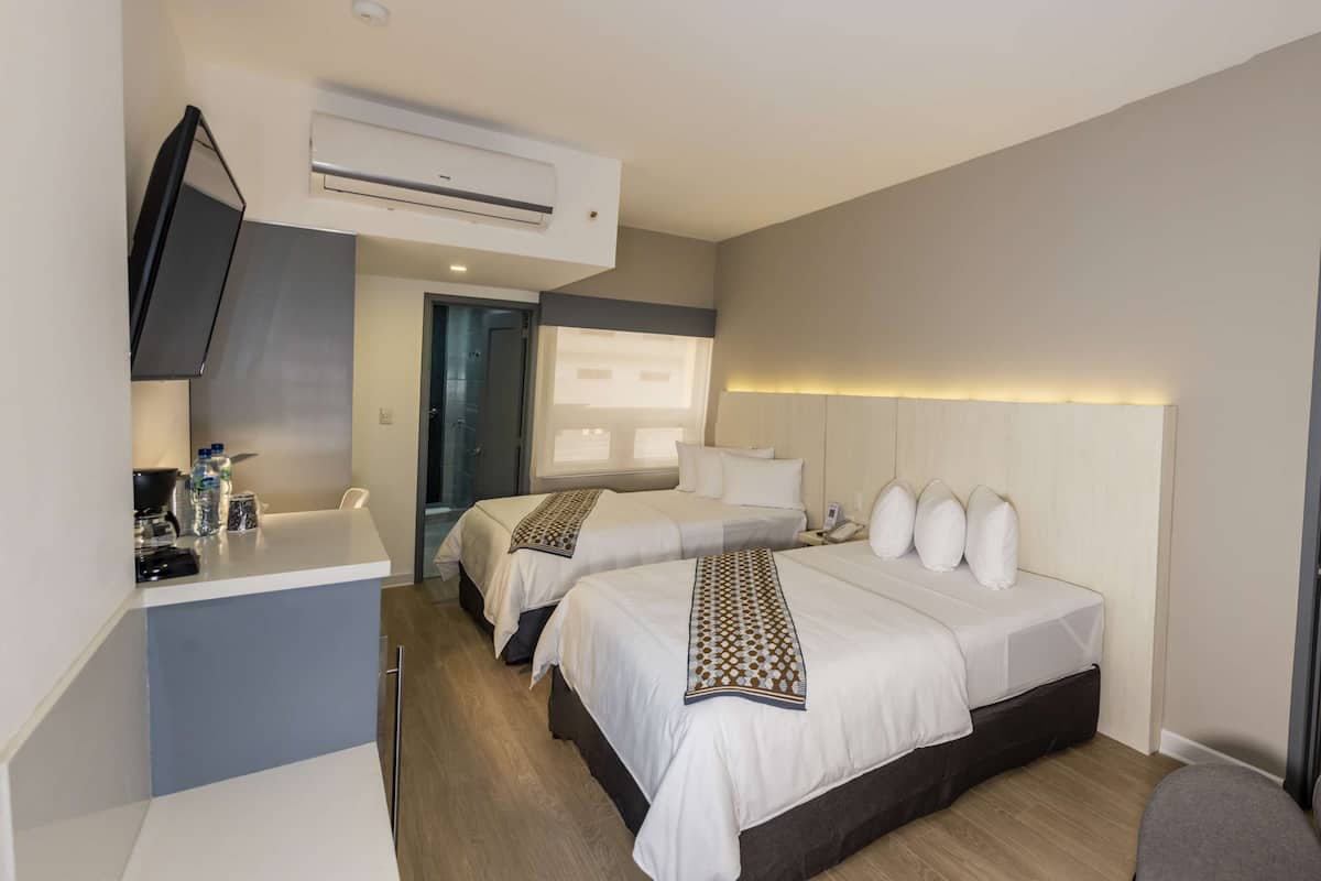 Een hotelkamer met twee bedden, een bureau met een flatscreen televisie, een koffiezetapparaat en een minibar.