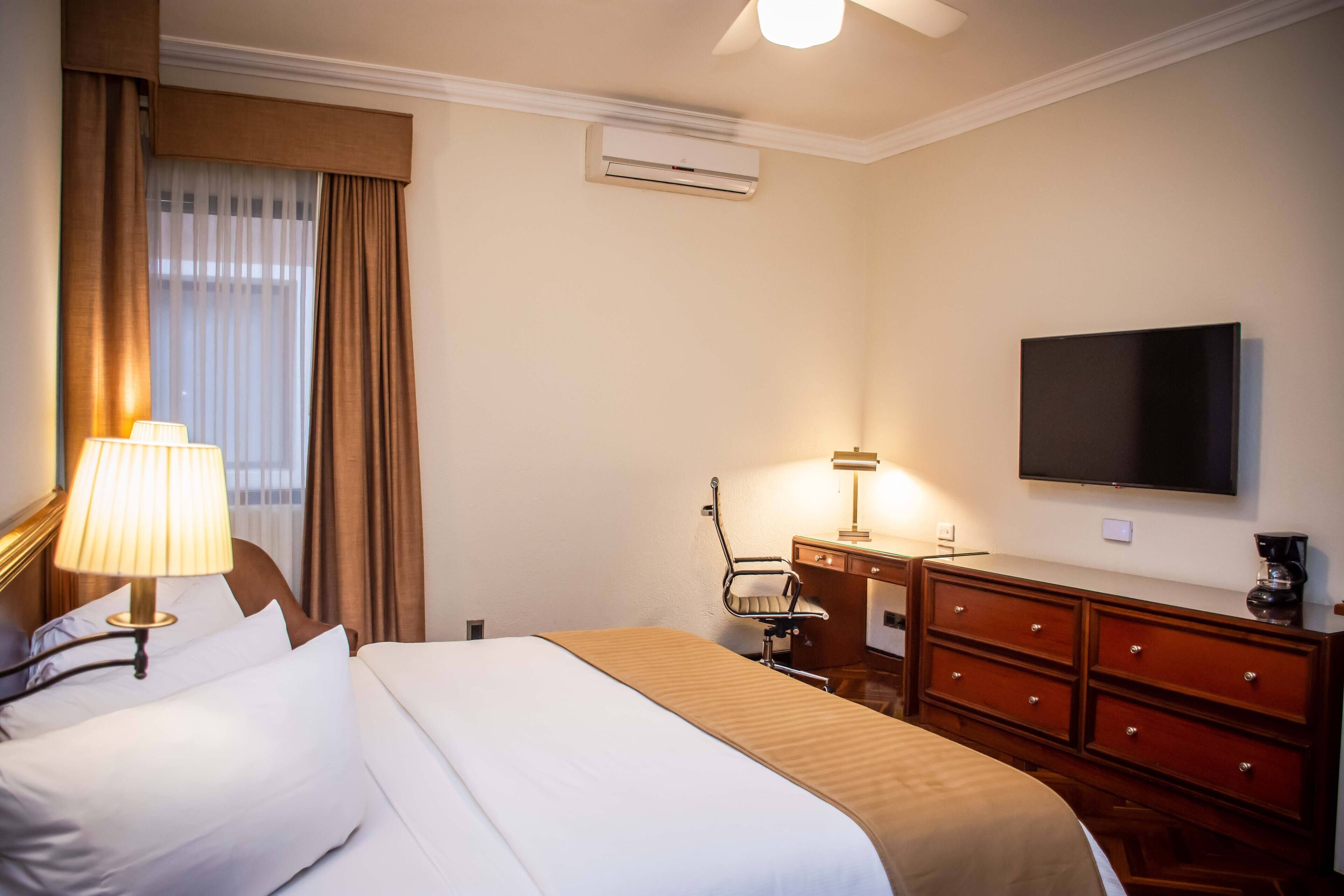 Una habitación de hotel con cama, escritorio, silla, televisión y cómoda.
