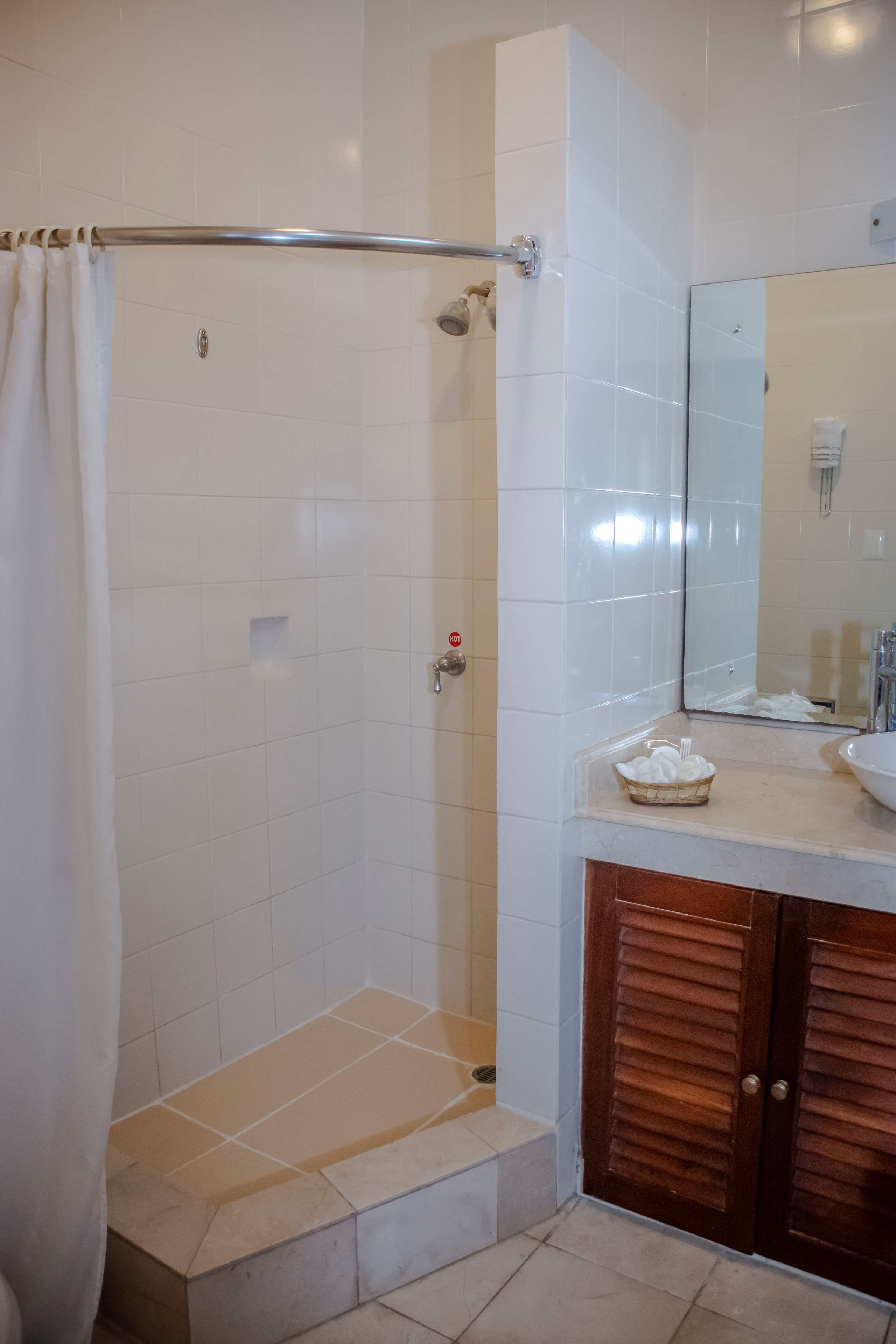 Un baño con azulejos blancos, ducha con puerta de vidrio, tocador de madera con lavamanos y un perchero para toallas.