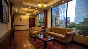 A spacious lobby with a sofa, armchairs, a coffee table, and a large window offering a view of modern buildings and greenery.