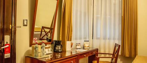 A hotel room with a wooden desk, a chair, a bed, a television, and a window with curtains.
