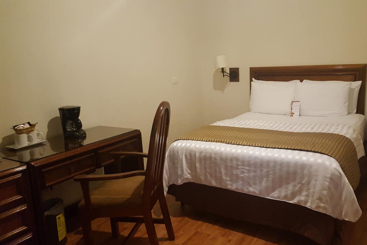 Een hotelkamer met een bed, bureau, stoel, nachtkastje en een lamp.