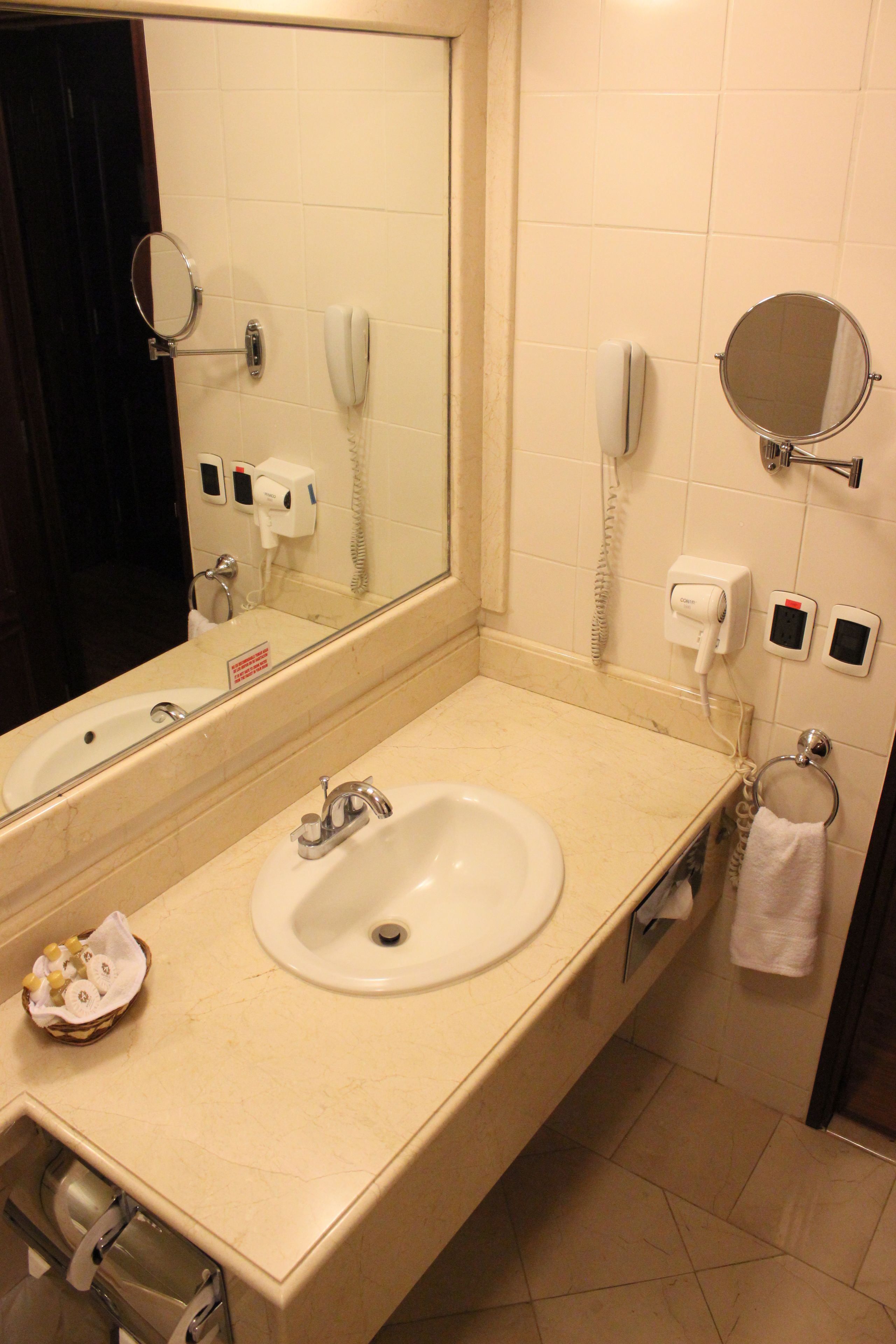 A bathroom with a sink, mirror, and two phones mounted on the wall.