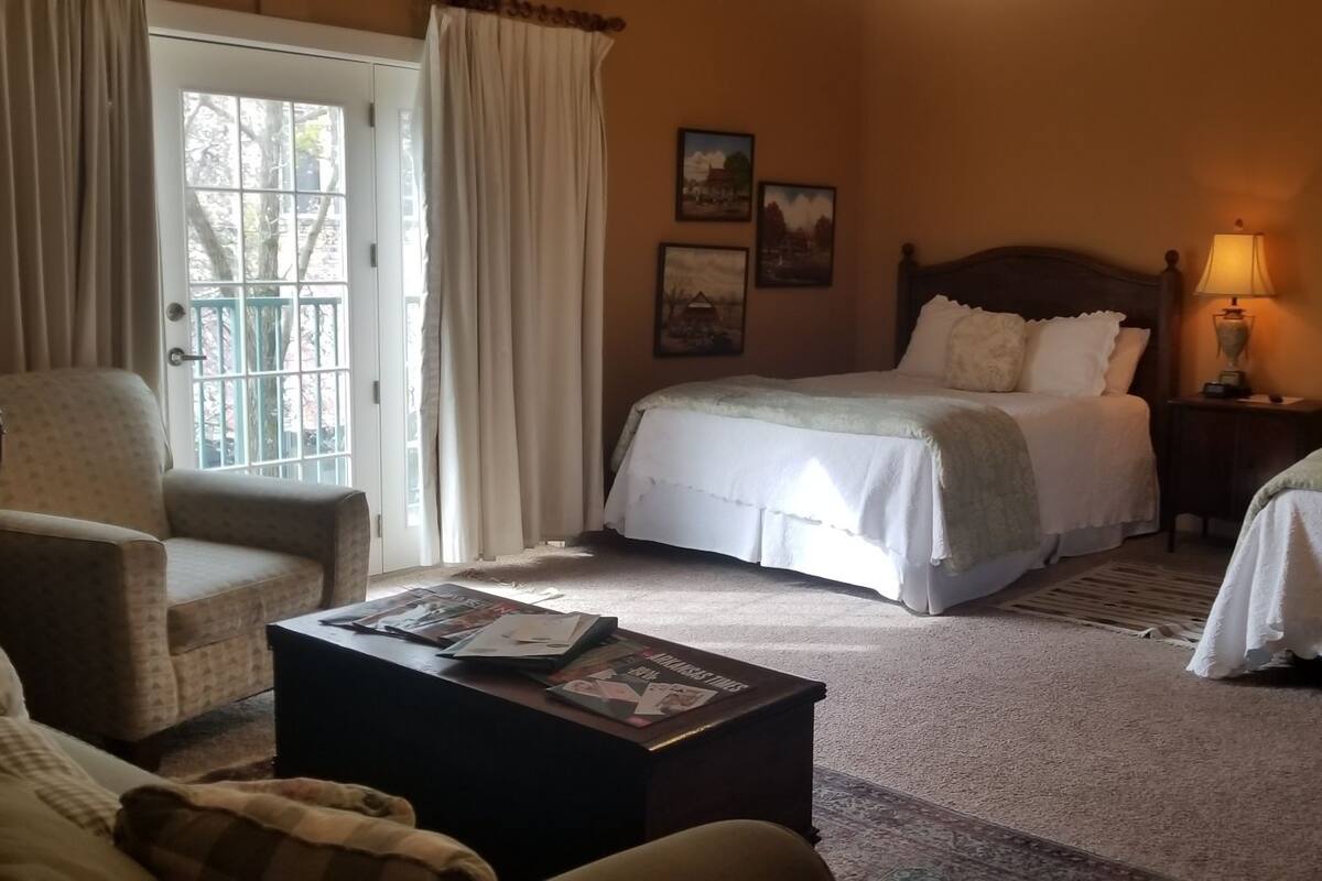 A bedroom with two beds, a chair, a table with magazines, and a lamp.