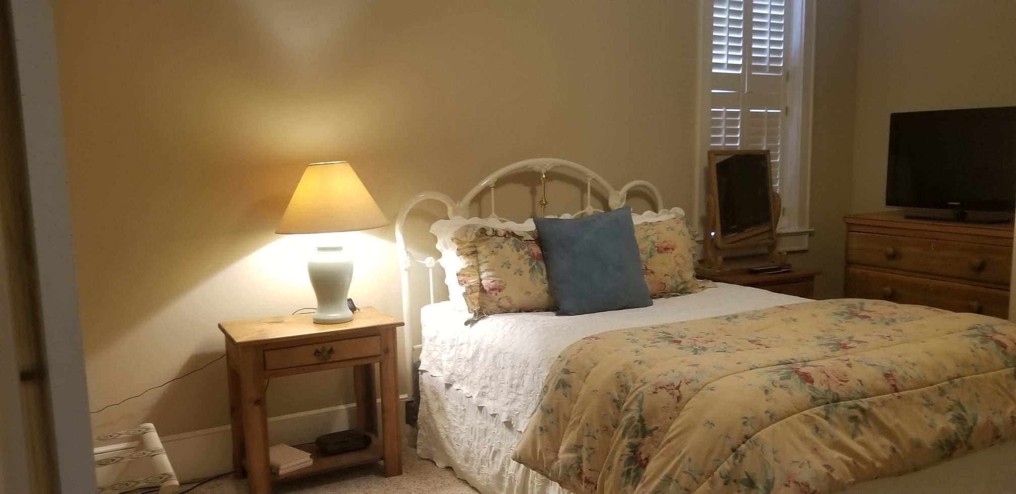 Un dormitorio con cama, mesita de noche con lámpara, cómoda y televisor.