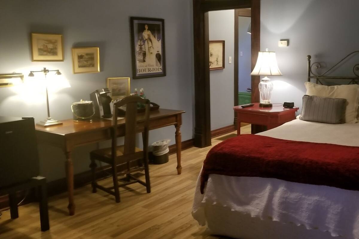 A neatly arranged bedroom with a bed, bedside table, lamp, chair, and desk.