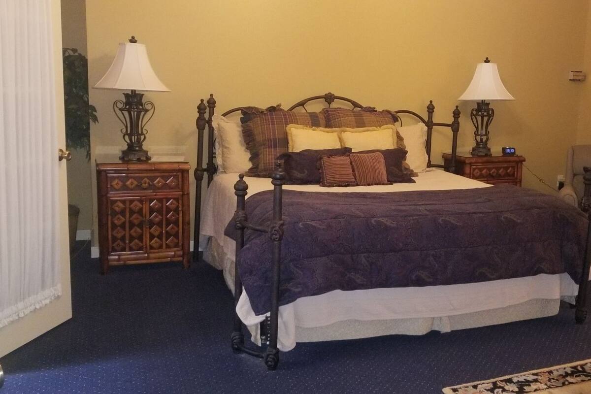 A bedroom with a four-poster bed, two bedside tables with lamps, a chair, a small table, and a framed picture on the wall.