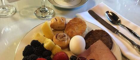 A breakfast plate with fruits, pastries, and ham. There are two cups of coffee and a glass of orange juice on the table.