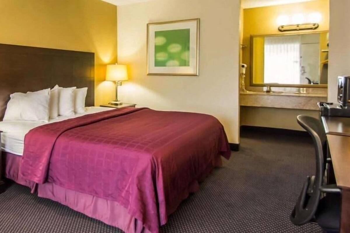 A hotel room with a bed, a desk, a chair, a lamp, a mirror, and a television.