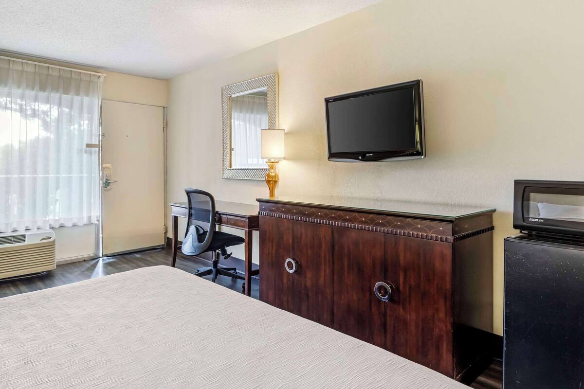 A hotel room with a bed, a desk, a chair, a TV, a dresser, and a window with curtains.