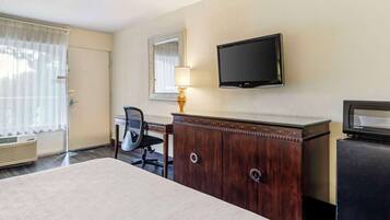 Quarto de hotel com cama, escrivaninha, cadeira, televisão, cómoda e janela com cortinas.