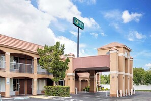 Quality hotel with a two-story structure and flat roof, set amidst a peaceful environment with a parking lot and lush greenery.