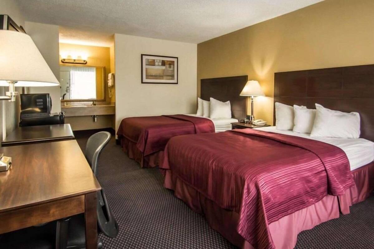 Una habitación de hotel con dos camas, un escritorio, una silla, una lámpara y un espejo.