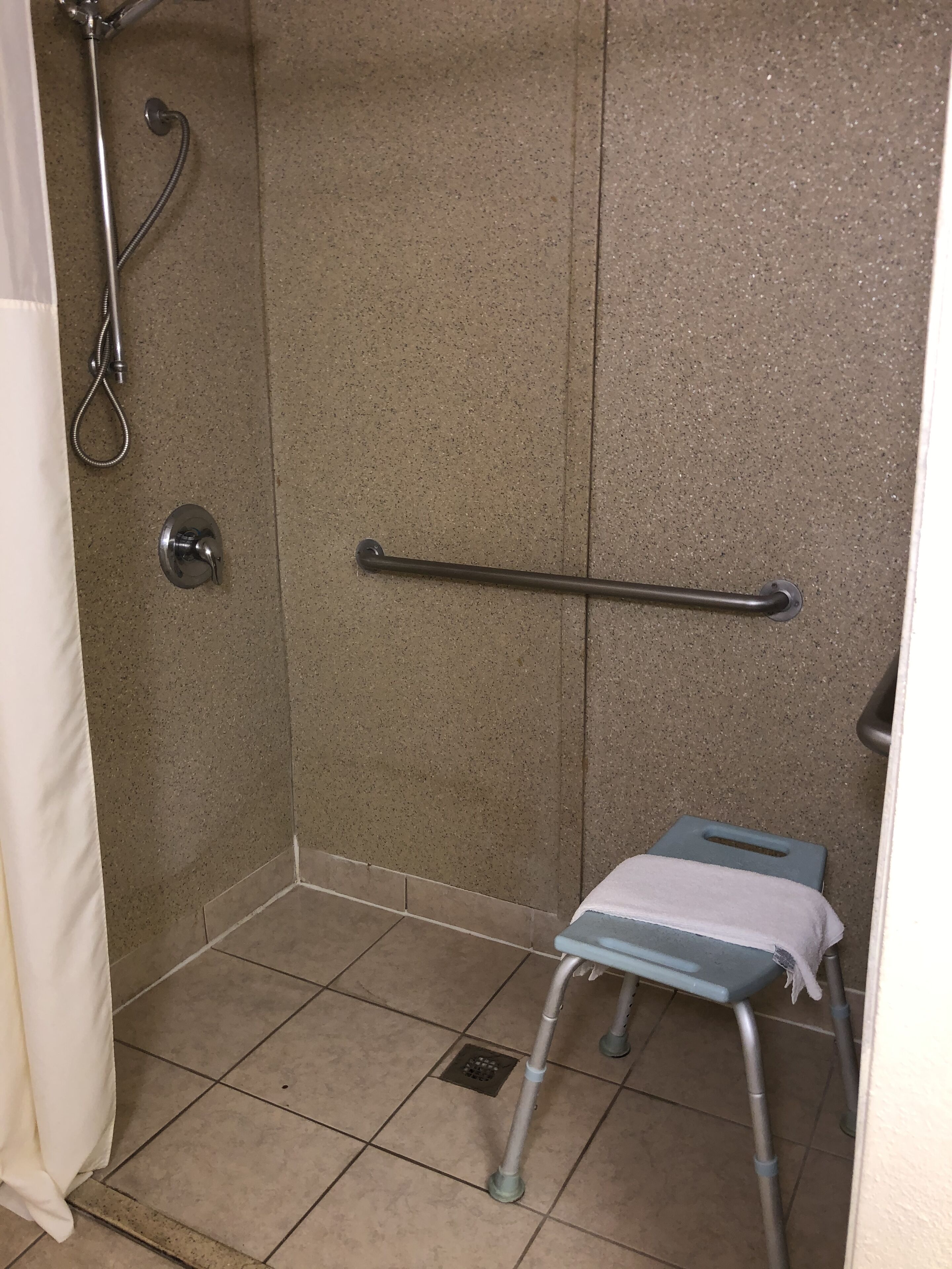 A shower area with a grab bar, a step stool, and a showerhead.