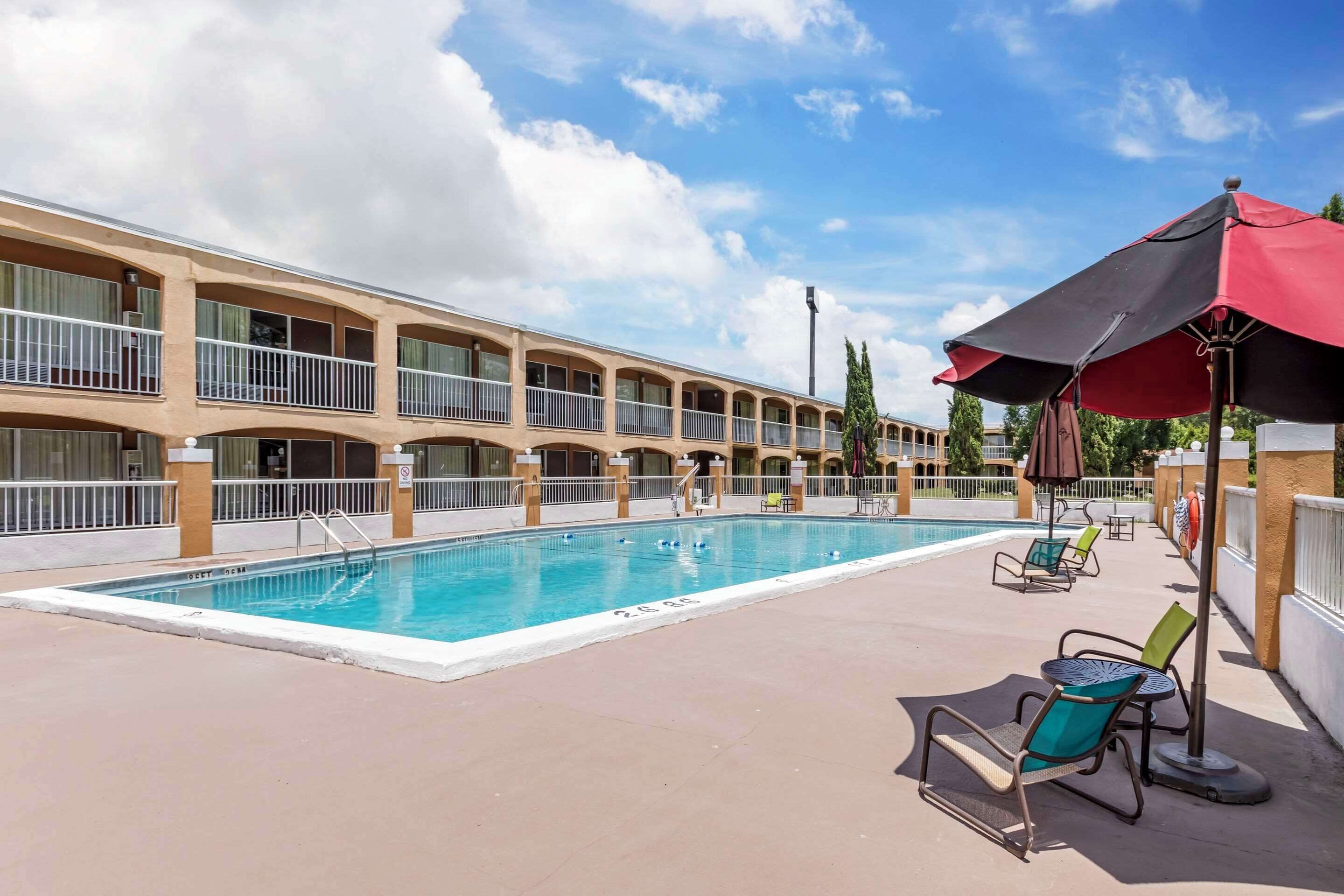 A hotel pool area with a swimming pool, lounge chairs, and umbrellas.