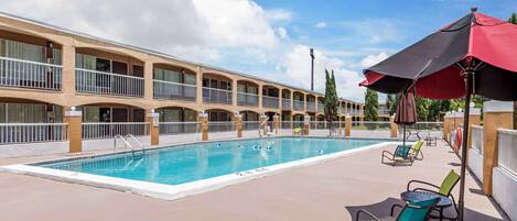 A hotel pool area with a swimming pool, lounge chairs, and umbrellas.