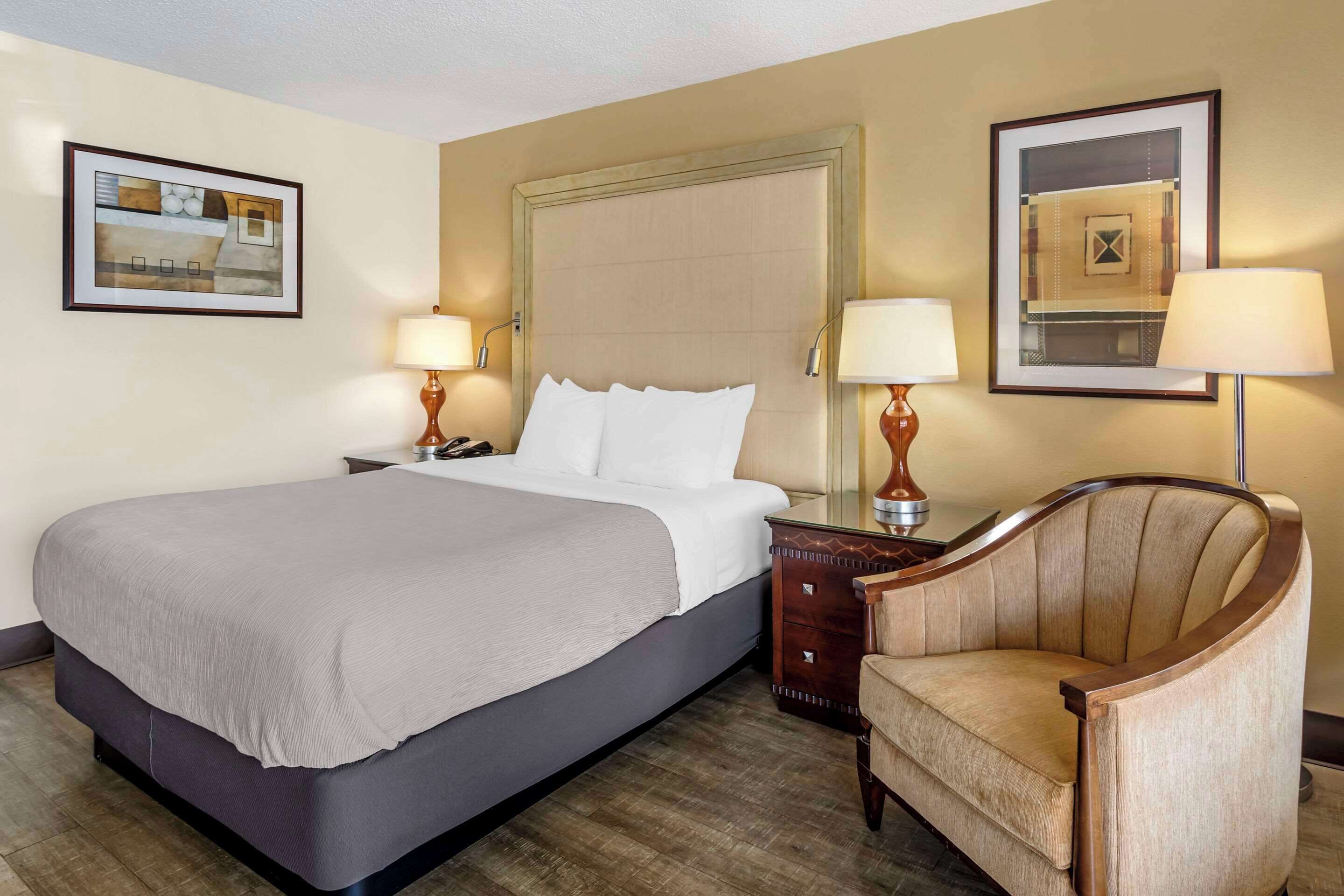 A hotel room with a large bed, two bedside tables with lamps, a chair, and framed artwork on the walls.