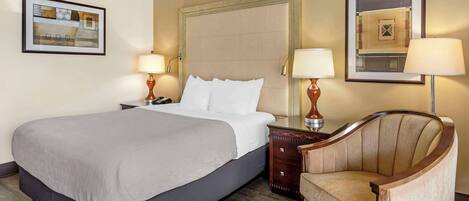A hotel room with a large bed, two bedside tables with lamps, a chair, and framed artwork on the walls.