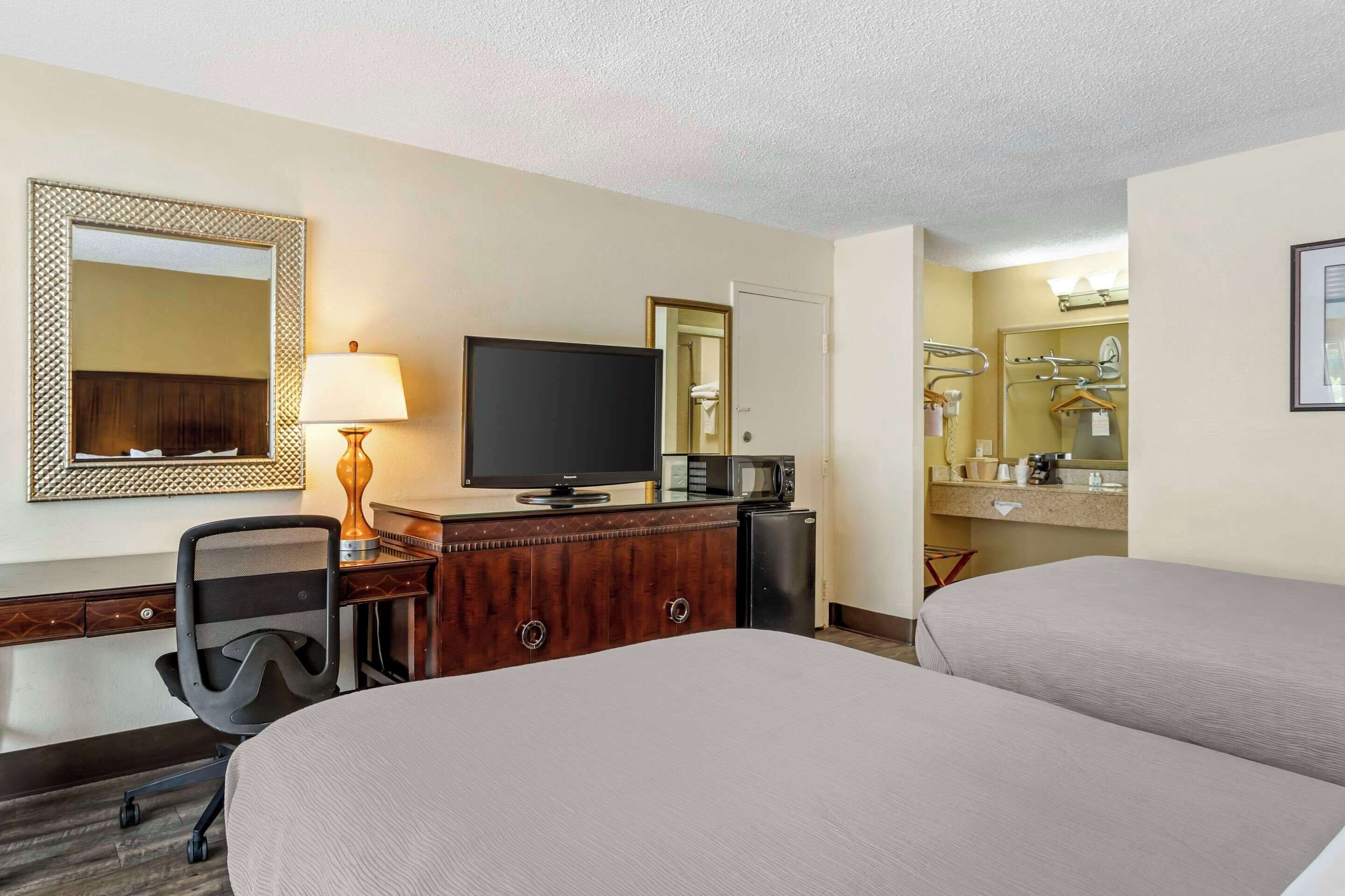 A hotel room with two beds, a desk with a television, a lamp, a microwave, and a small refrigerator.