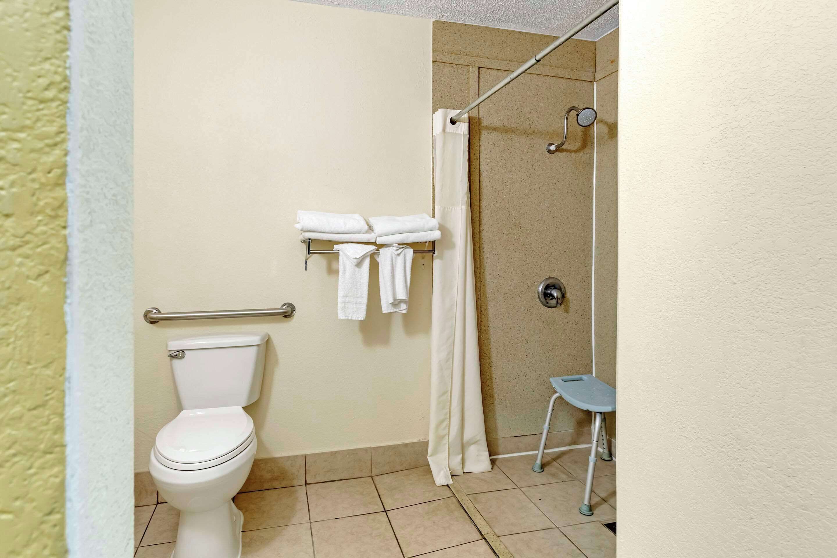 A bathroom with a toilet, a shower with a glass door, and a small stool.