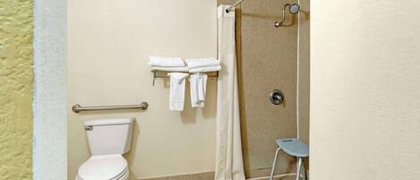 A bathroom with a toilet, a shower with a glass door, and a small stool.