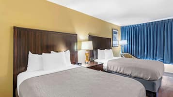 A hotel room with two beds, a nightstand with a lamp, a chair, and a large window with curtains.