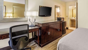 Ein Hotelzimmer mit einem Bett, einem Schreibtisch mit Stuhl, einem Fernseher, einem Spiegel und einem Kleiderschrank.