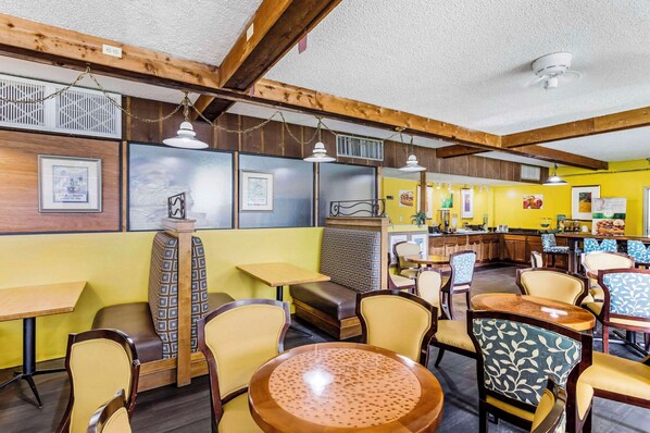A restaurant with wooden beams, yellow walls, and patterned chairs. Tables and a counter are visible.
