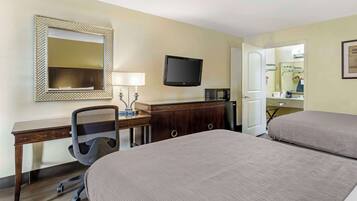 A hotel room with two beds, a desk with a chair, a television, a microwave, and a bathroom visible through an open door.