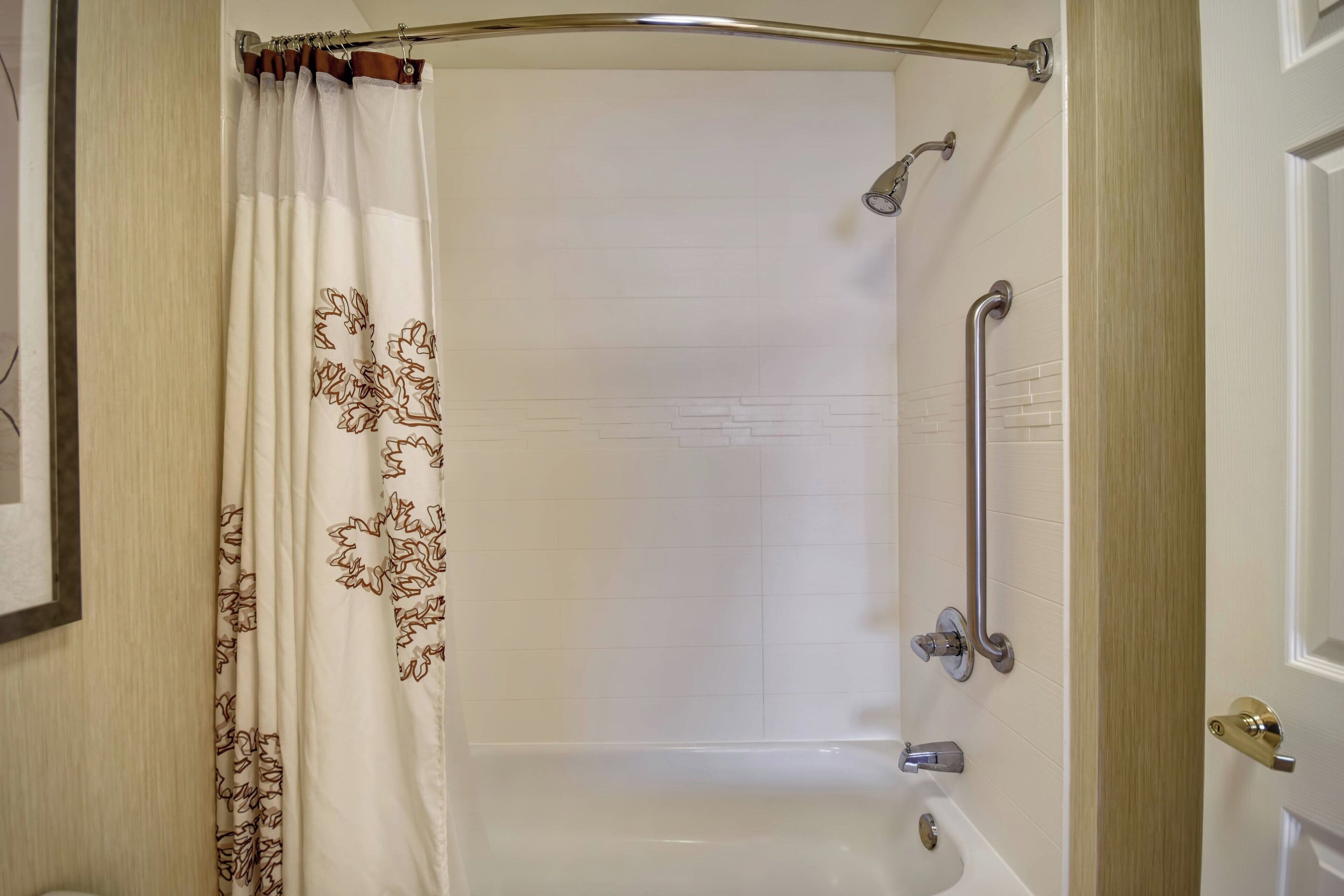 A bathroom with a shower, a grab bar, and a door with a brass handle.