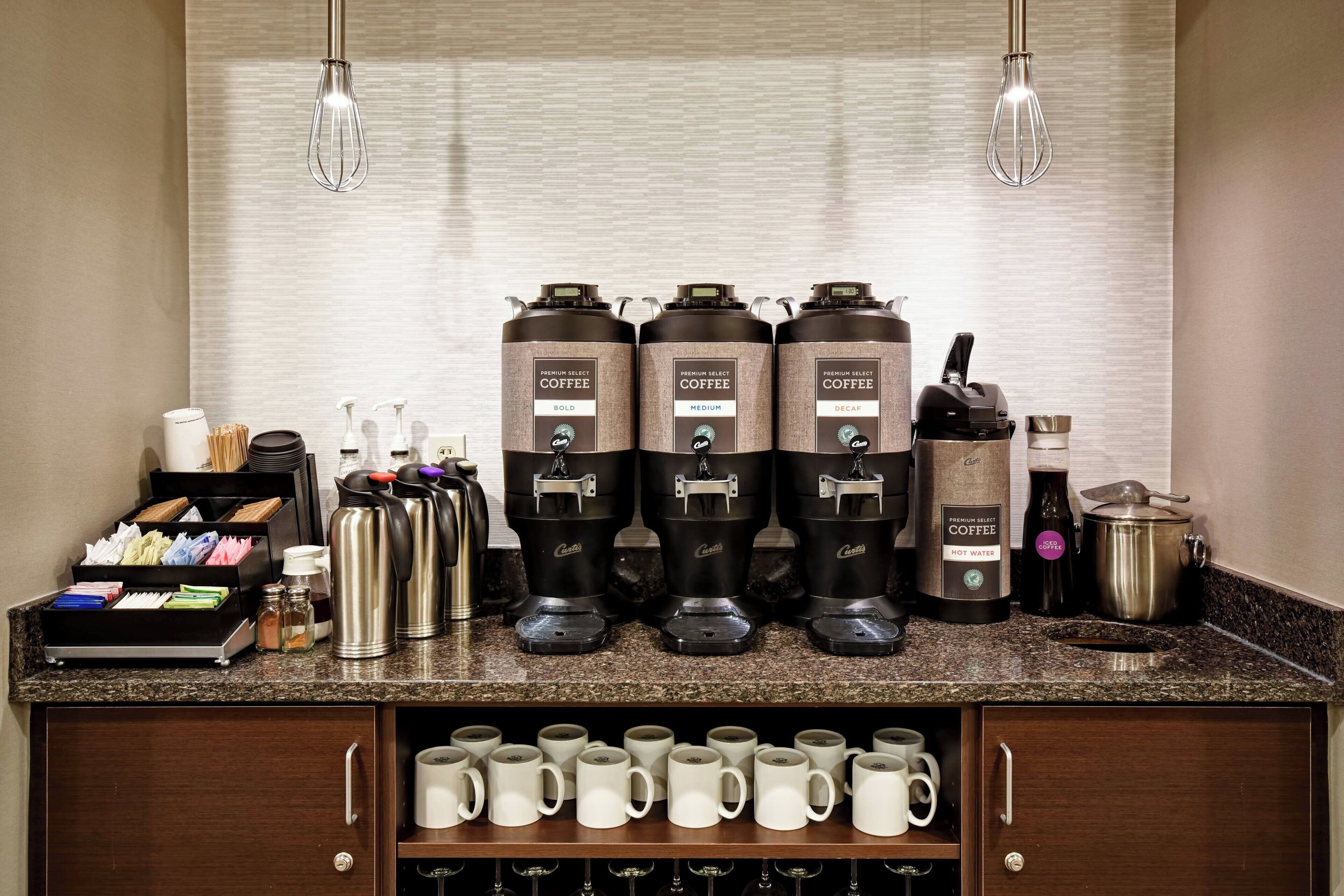 Eine Kaffeestation mit drei Kaffeemaschinen, einer Kaffeekanne sowie verschiedenen Tassen und Besteck.
