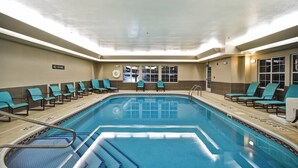 Uma piscina com azulejos azuis, um aviso de 'NÃO MERGULHAR' e cadeiras verde-água nas bordas.