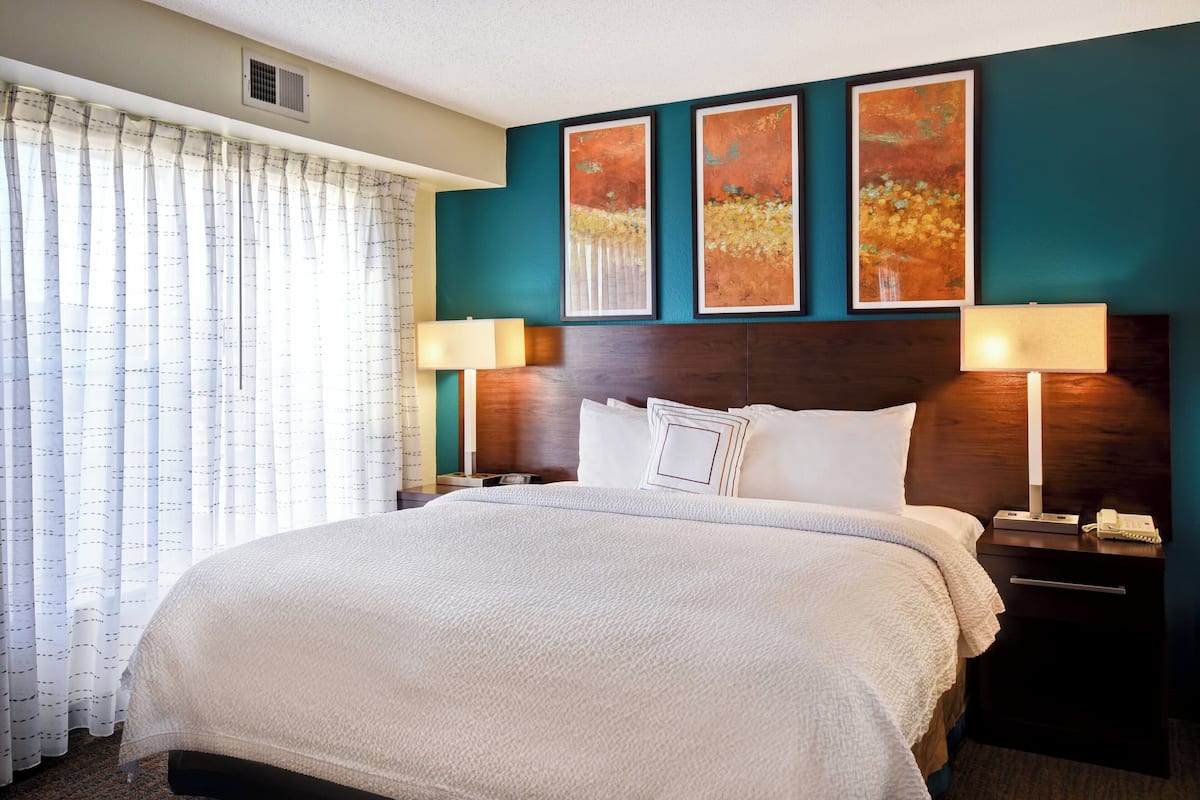 A hotel room with a large bed, two bedside tables, a nightstand, and a window with curtains.